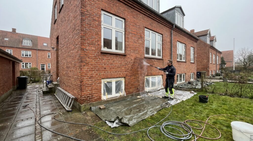overlap-facade, facade_masonry, work, outdoor, facade,murværk,omfugning,pudsning,sandblæsning,sokkel,mursten,renovering, Håndværker renser en ældre facade med afdækning omkring vinduer og havefliser., på et ældre byhus med små danske vinduer., dansk bolig, håndværk, renovering, vedligeholdelse, pris, tilbud, facade_masonry, work, outdoor, facade,murværk,omfugning,pudsning,sandblæsning,sokkel,mursten,renovering