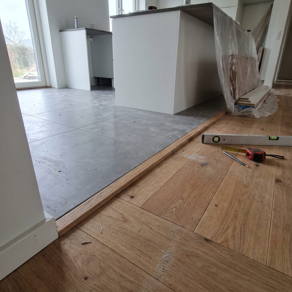 overlap-gulv, floor_surface, detail, indoor, gulv,fliser,klinker,trægulv,vinyl,epoxy,belægning,overflade,vedligehold, Nærbillede af overgang mellem klinkegulv og trægulv med pæn afslutning., i et dansk køkken-alrum., dansk bolig, håndværk, renovering, vedligeholdelse, pris, tilbud, floor_surface, detail, indoor, gulv,fliser,klinker,trægulv,vinyl,epoxy,belægning,overflade,vedligehold