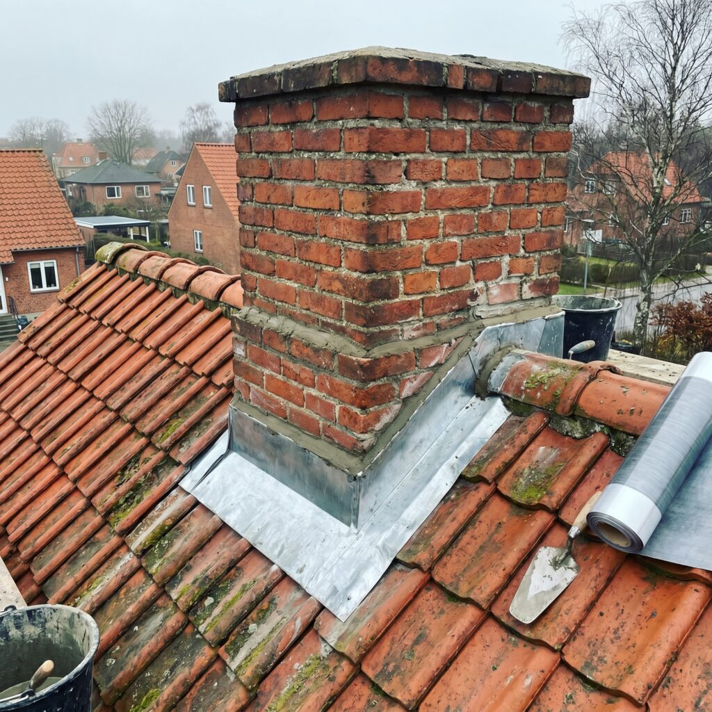 overlap-tag, roof_chimney, detail, outdoor, tag,skorsten,tagrender,inddækning,tagsten,rygning,vedligehold,reparation, Nærbillede af tagsten, inddækning og fuge omkring en muret skorsten., på et ældre hus med muret skorsten., dansk bolig, håndværk, renovering, vedligeholdelse, pris, tilbud, roof_chimney, detail, outdoor, tag,skorsten,tagrender,inddækning,tagsten,rygning,vedligehold,reparation